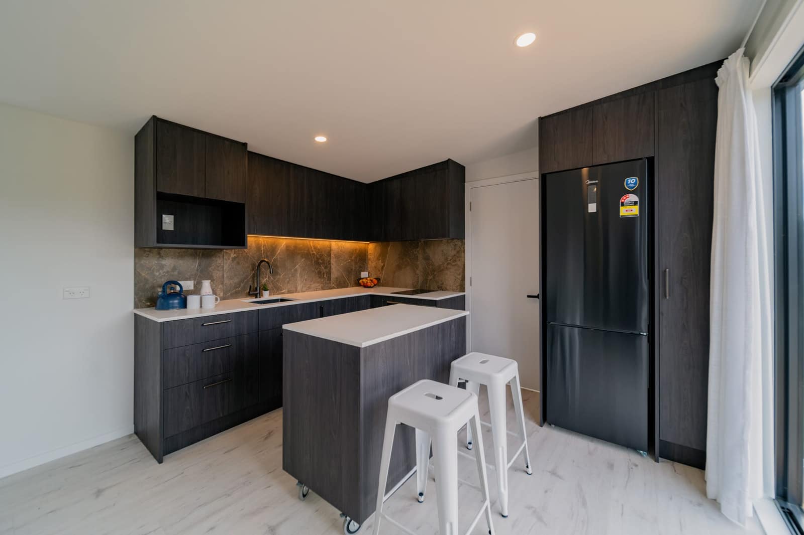 Kitchen with island, integrated fridge and dark joinery